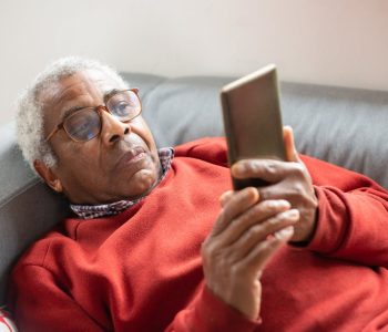 senior man laying on couch looking at phone