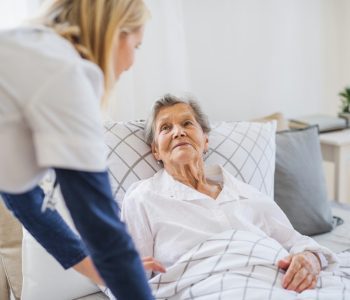 female caregiver leaning over senior in bed