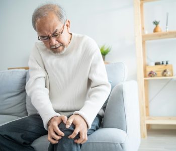 senior man on sofa suffering from knee joint paint